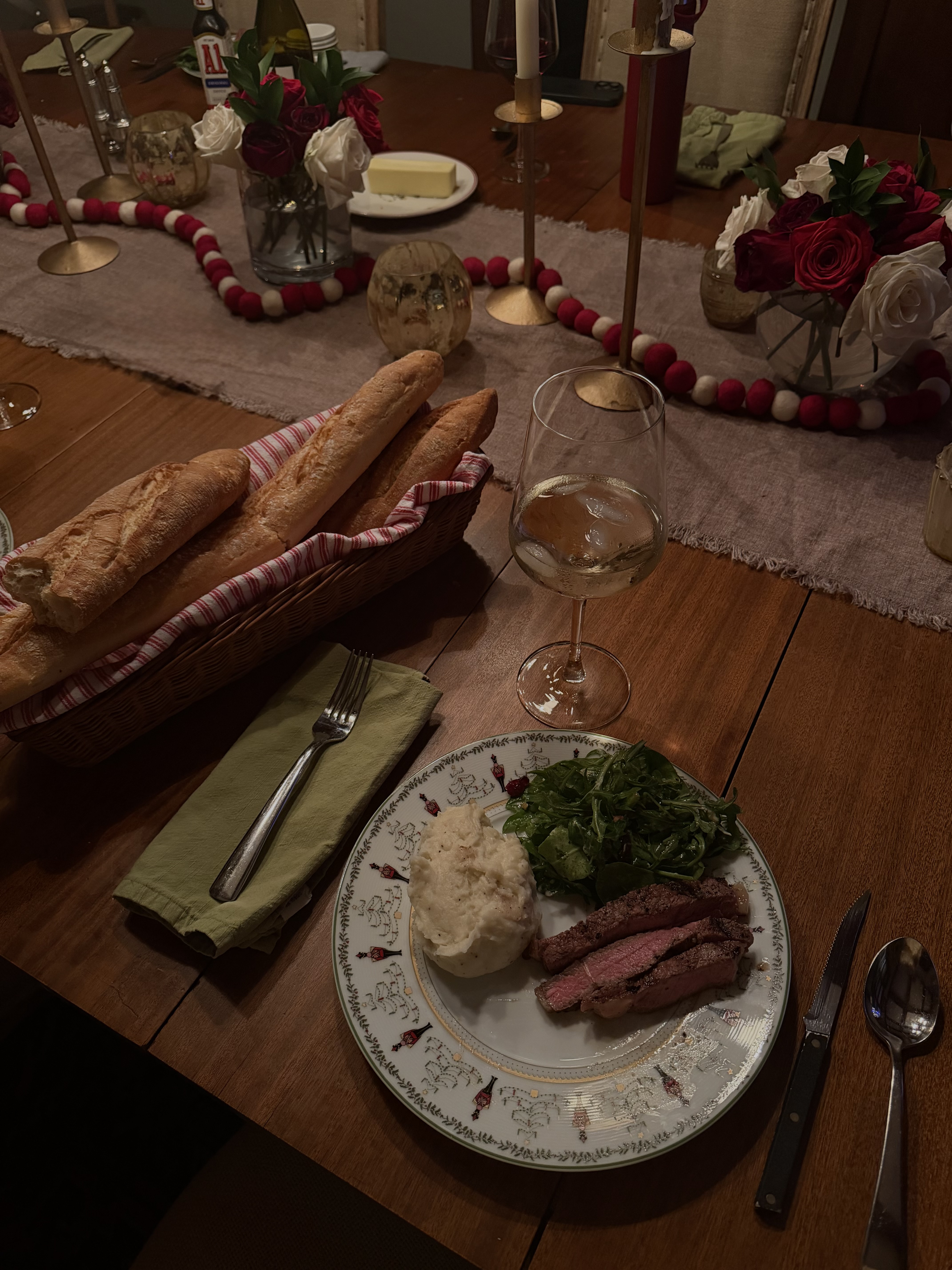 A candlelit dinner table set with roses, bread, and steak
